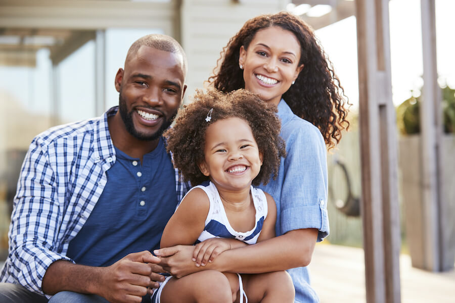 A Black mom and dad embrace their adorable little daughter while smiling outside