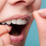 Closeup of a woman flossing her teeth with string floss against a blue background