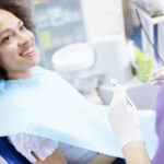 Black woman sits in the dental chair and smiles at her dental hygienist before her routine teeth cleaning