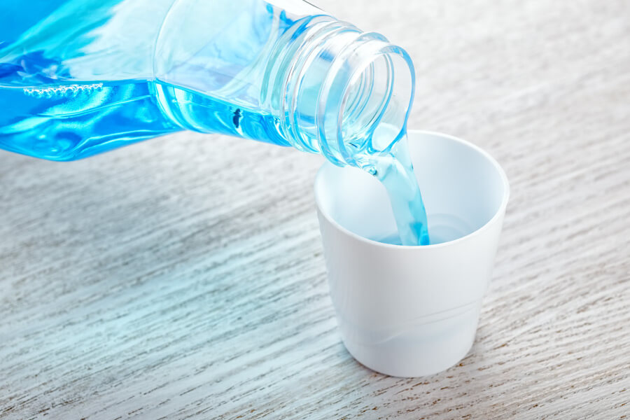 Closeup of a bottle of blue mouthwash being poured into a white cup